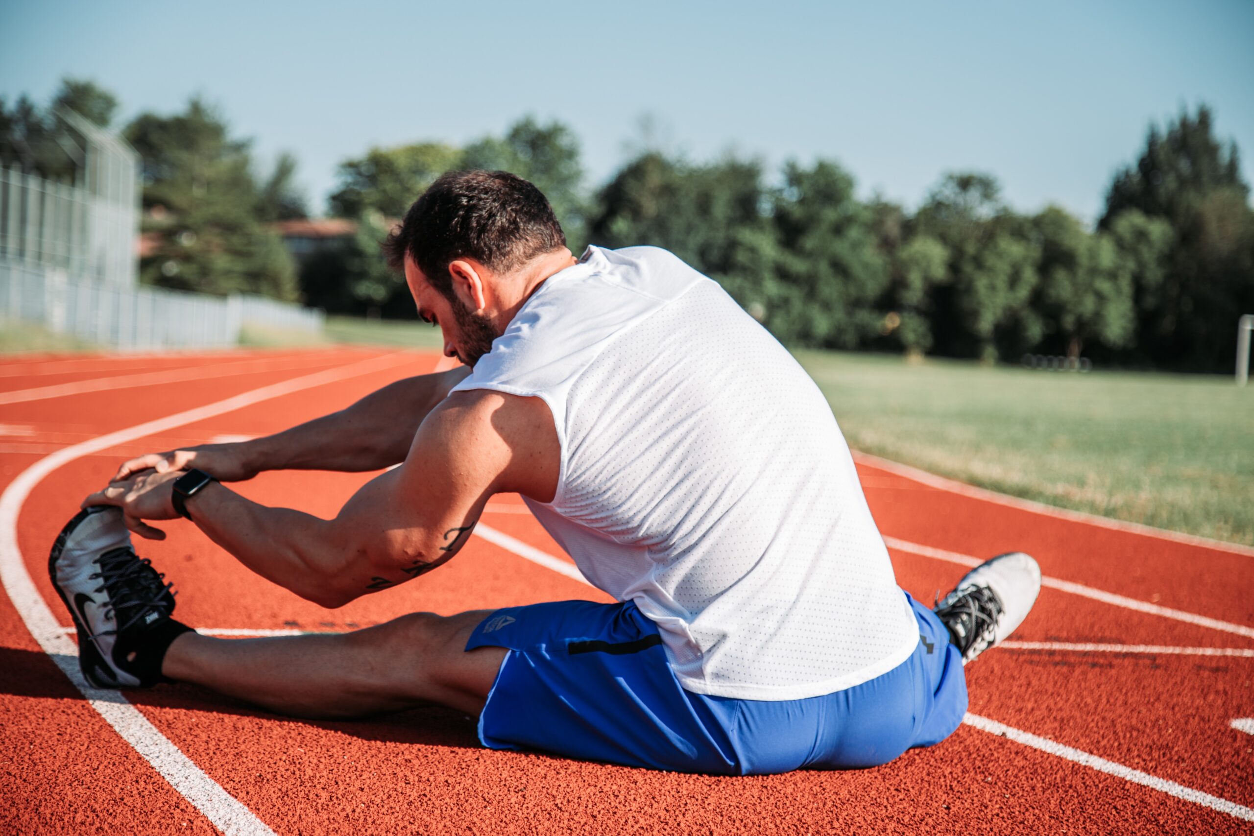 Man stretching his leg on a running track - sports and fitness